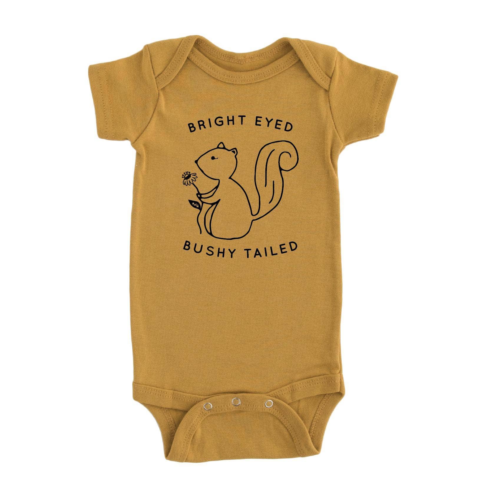 Mustard yellow baby onesie with a squirrel design and text that says bright eyed and bushy tailed on a white background