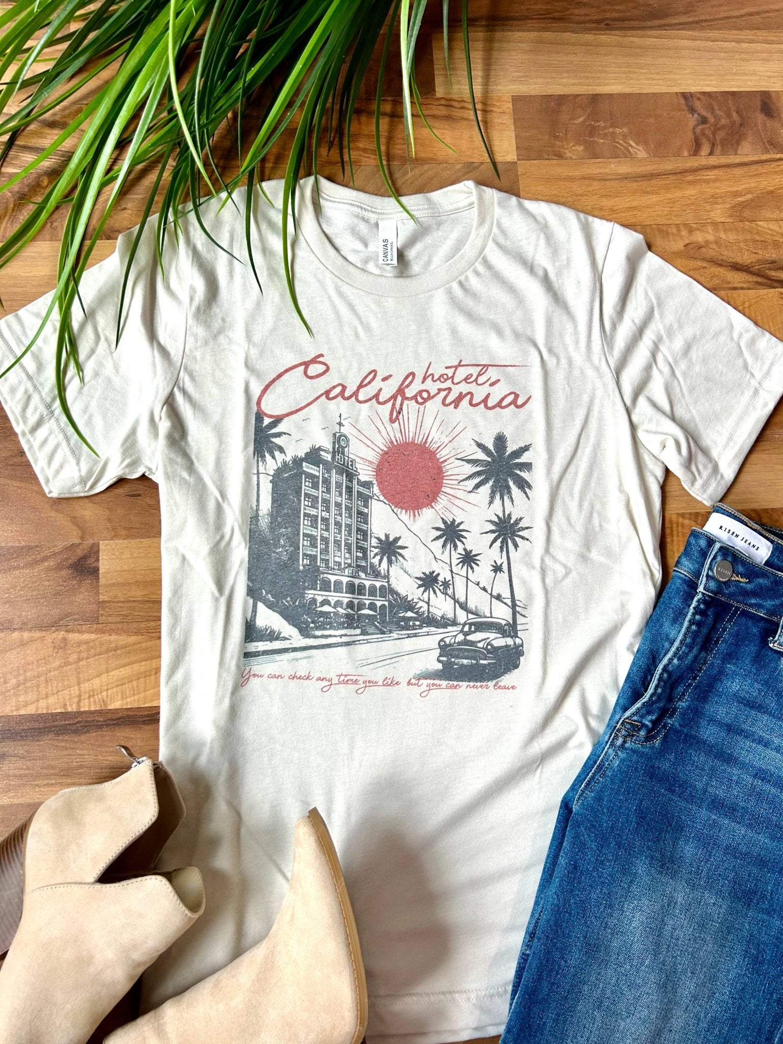 White t-shirt with 'California' graphic design on a wooden surface with jeans and shoes.