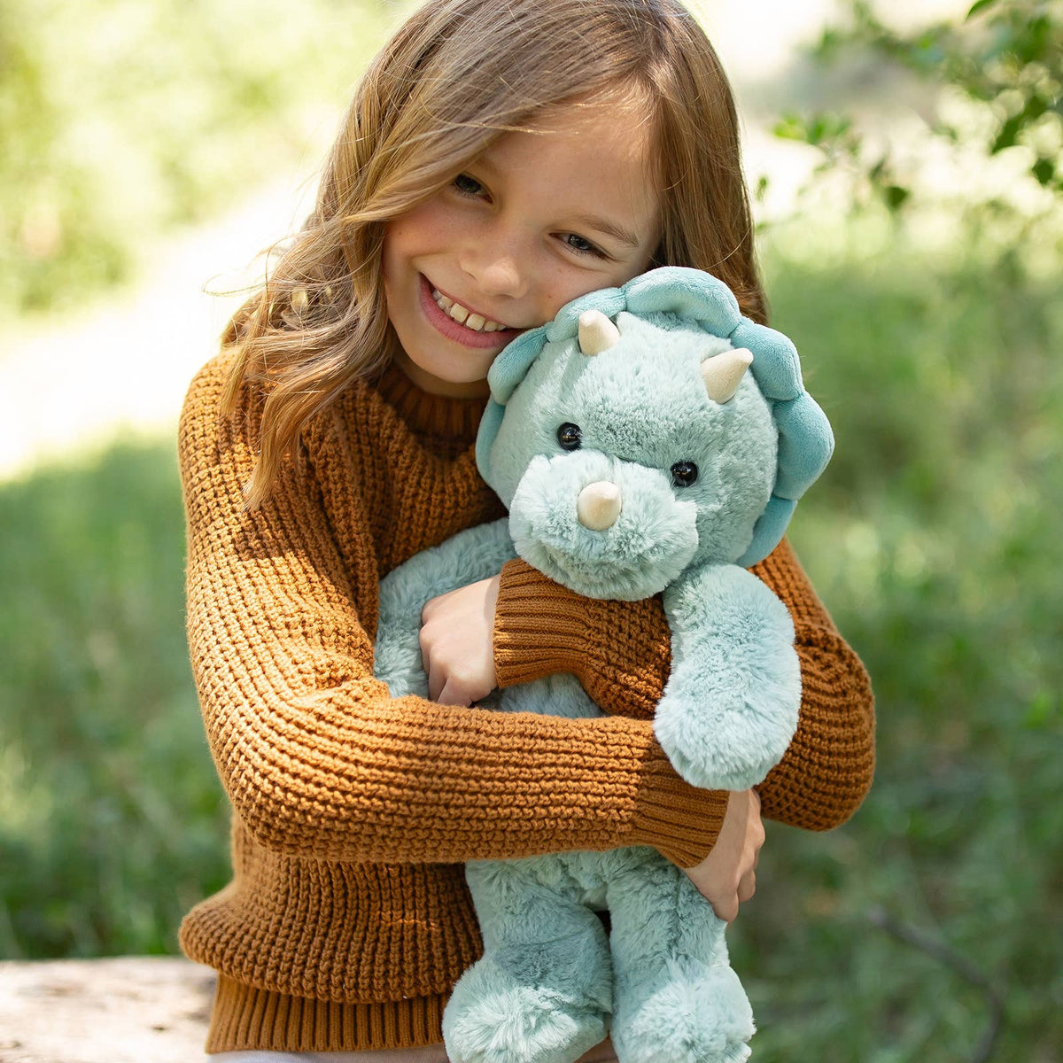 Child holding a plush dinosaur toy outdoors