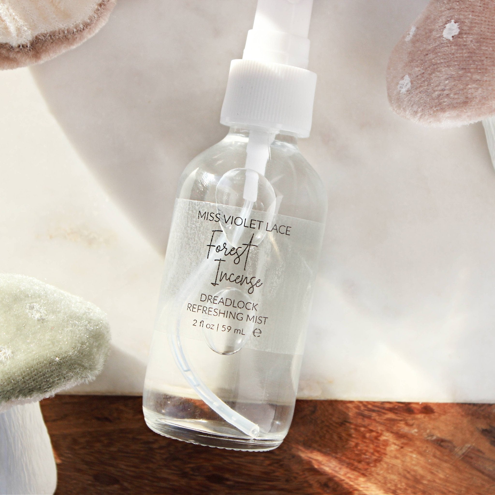 Miss Violet Lace Forest Incense Dreadlock Refreshing Mist in a clear 2 fl oz spray bottle, on a marble and wood surface.