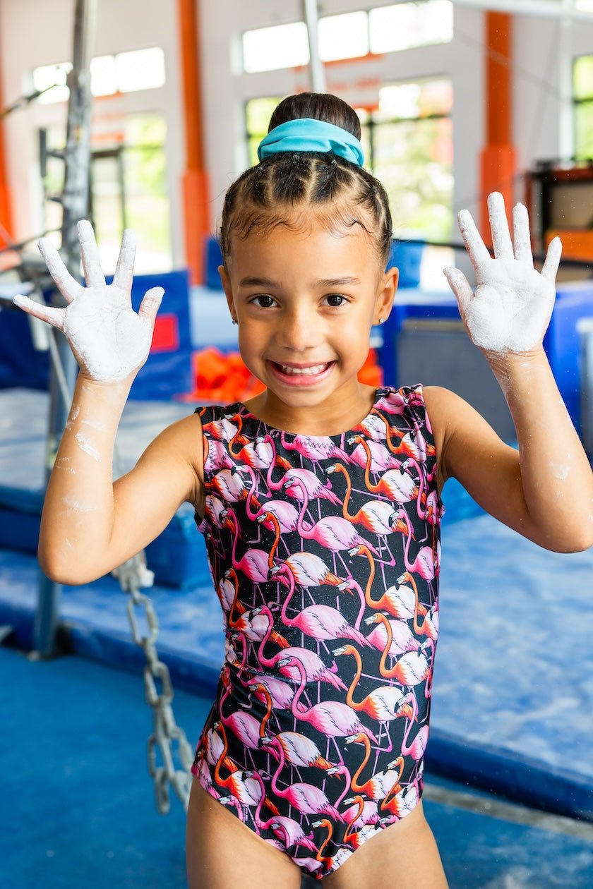 Young girl in a pink flamingo leotard with white gloves in a gymnasium setting