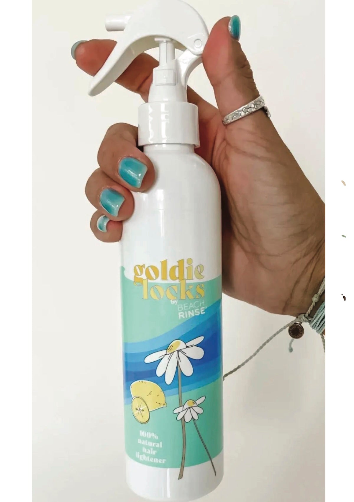 Hand holding a 'goldie locks' spray bottle with a floral design on a white background