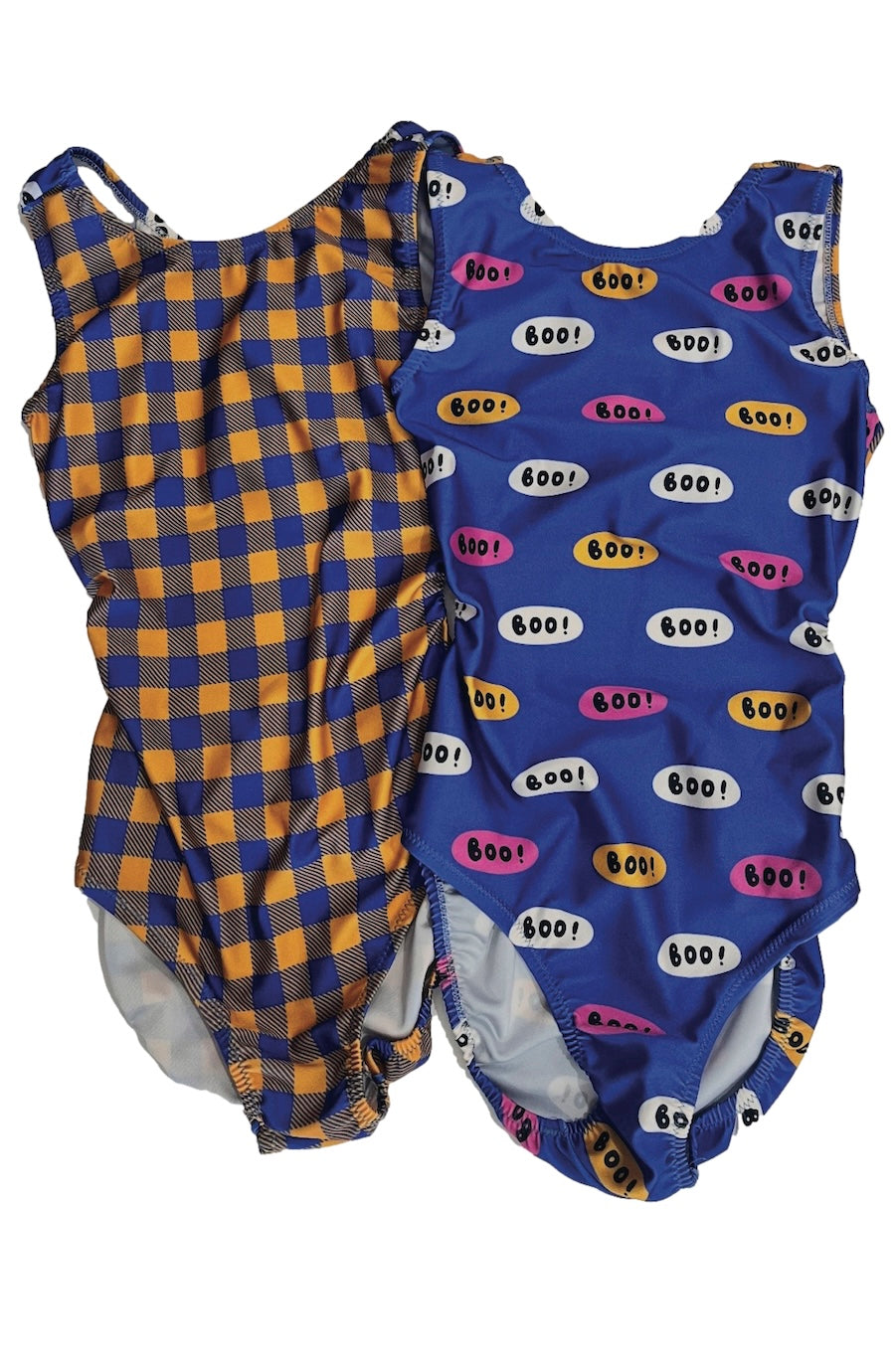 Two sleeveless baby leotards laid flat on a white background. The left gymnastics leotar has a blue and orange gingham plaid pattern, and the right leotard for girls has blue with a colorful pattern of speech bubbles containing 'boo!