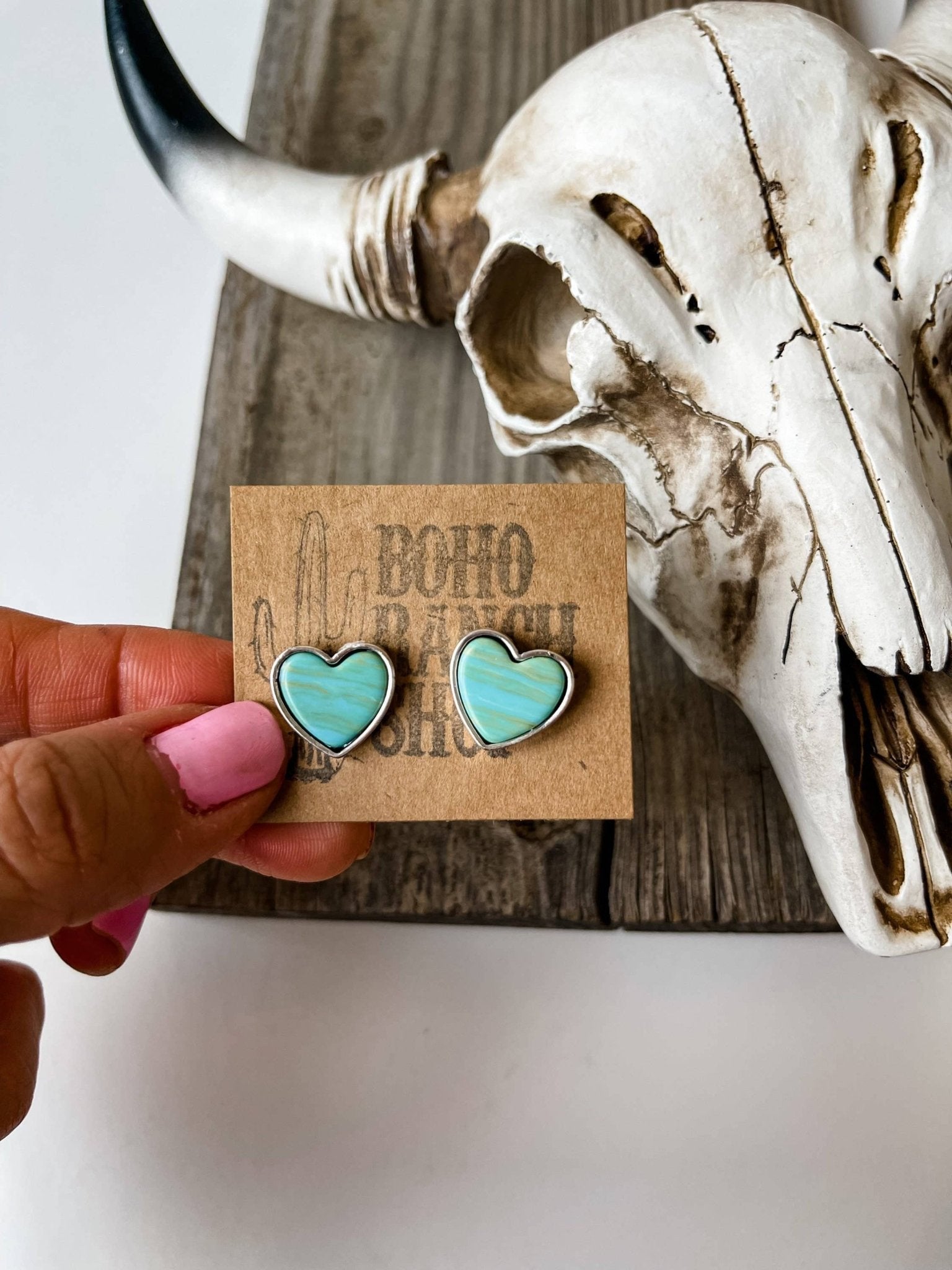 Turquoise heart-shaped earrings on a 'Boho' card with a skull in the background