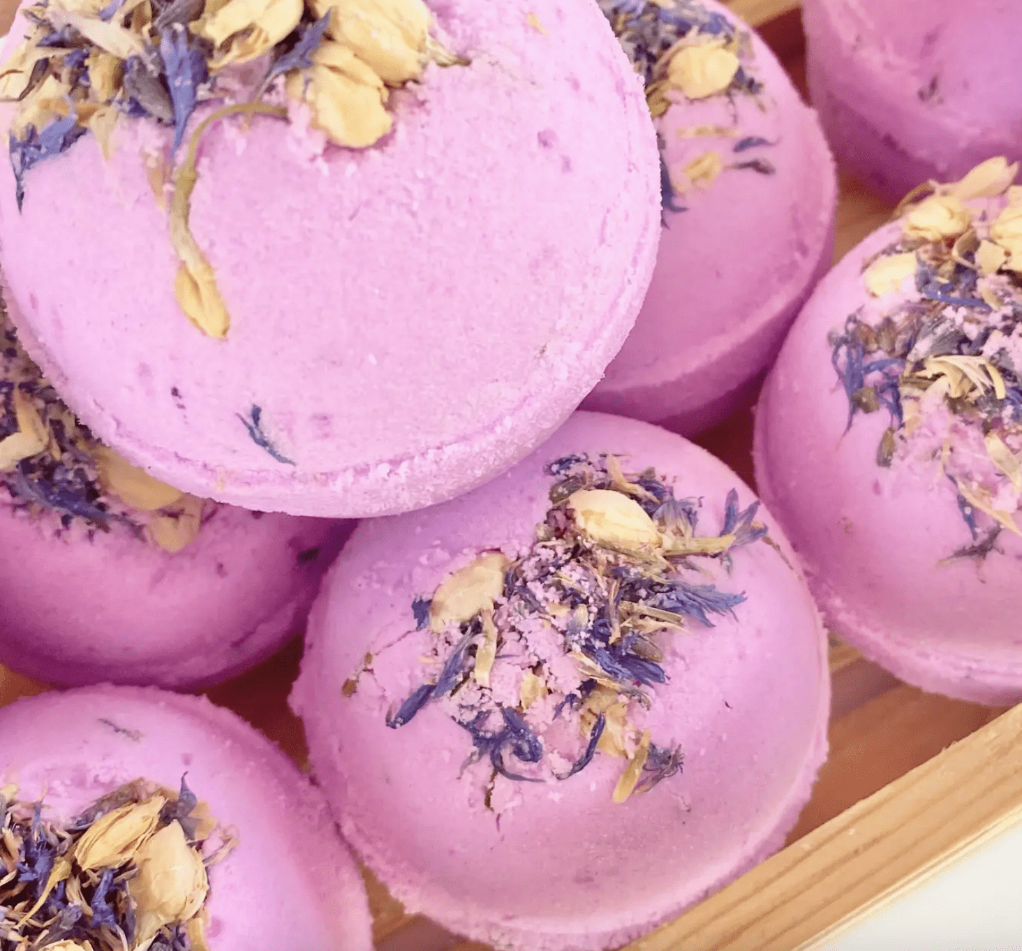 Purple bath bombs with dried flowers on a wooden surface