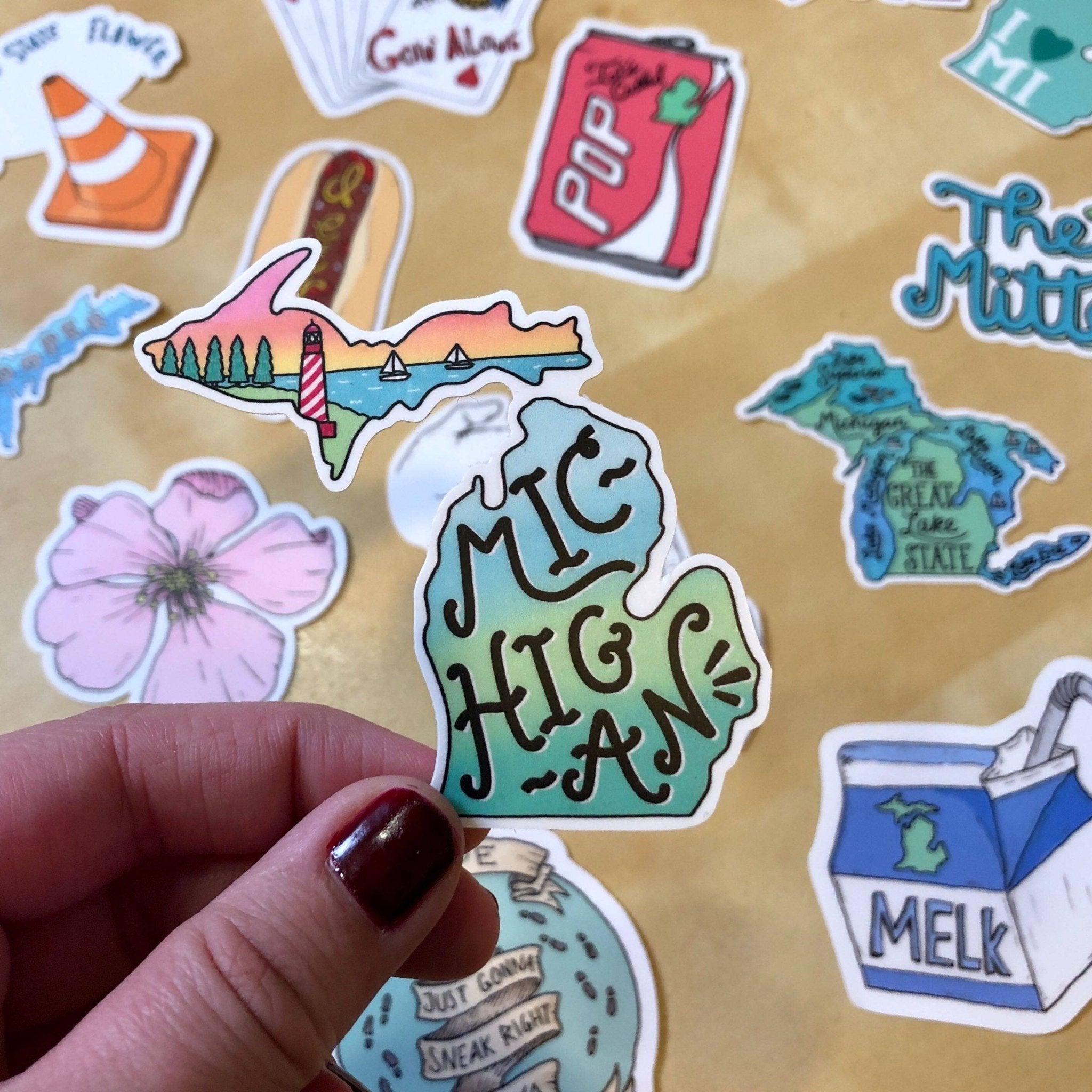 Michigan state shaped sticker with 'Michigan' written on it held in hand.