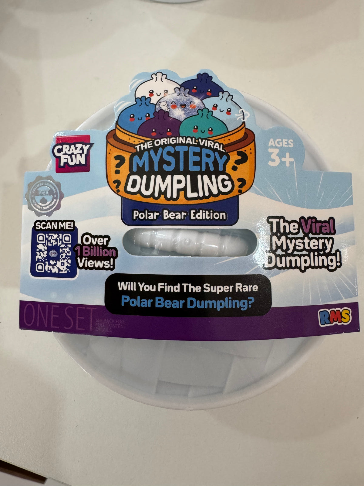A packaged novelty dumpling toy labeled 'The Original Viral Mystery Dumpling - Polar Bear Edition' on a white plastic tub, photographed on a light surface. The package includes cartoon polar bear graphics, a QR code, and branding for Crazy Fun and RMS.