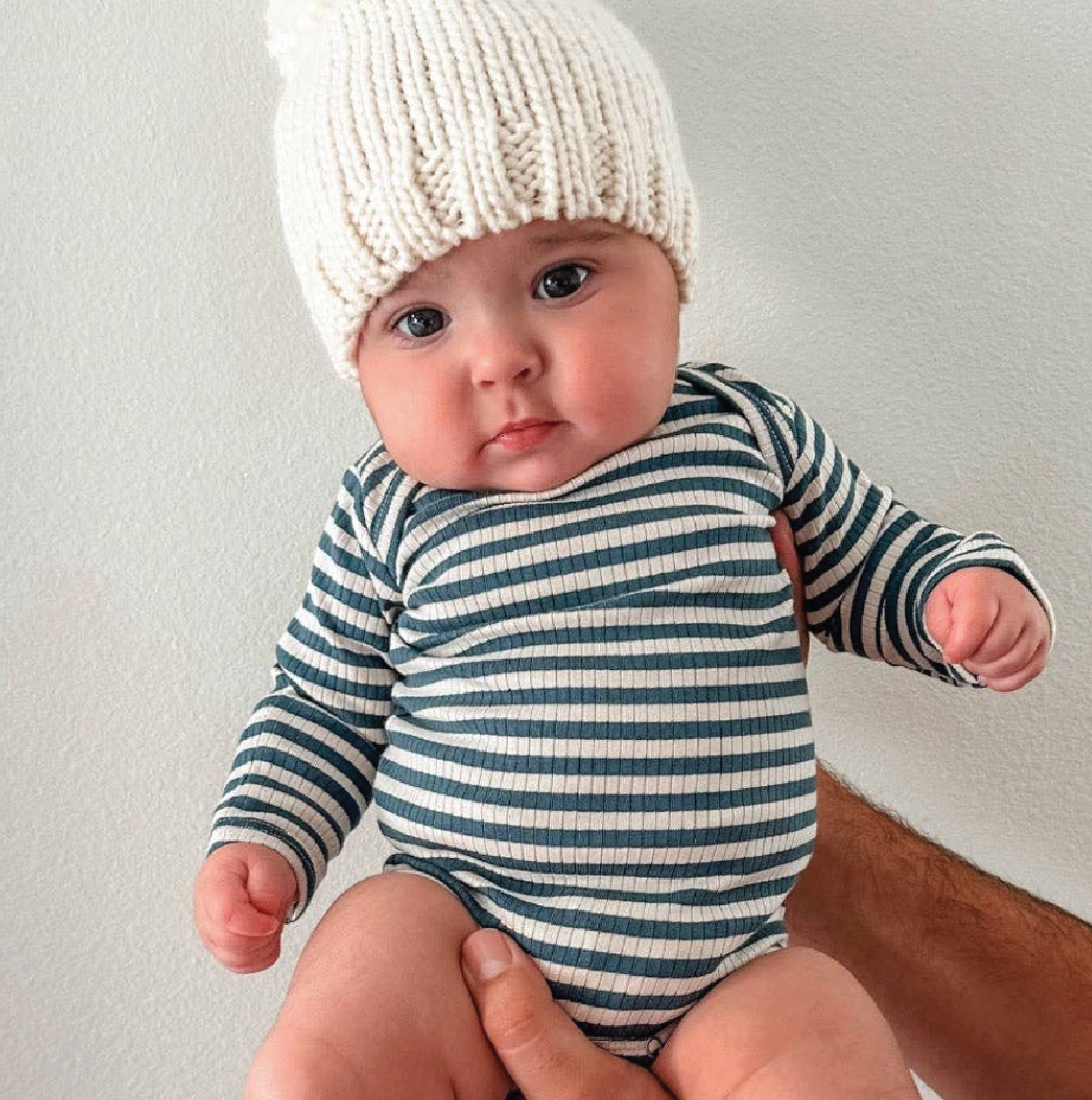 Baby wearing a striped onesie and white knit hat against a plain background