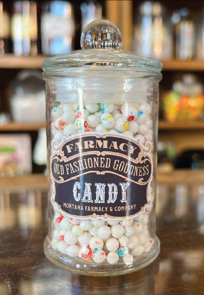 Glass jar filled with candy labeled 'Farmacy Old Fashioned Goodness Candy' on a reflective surface.