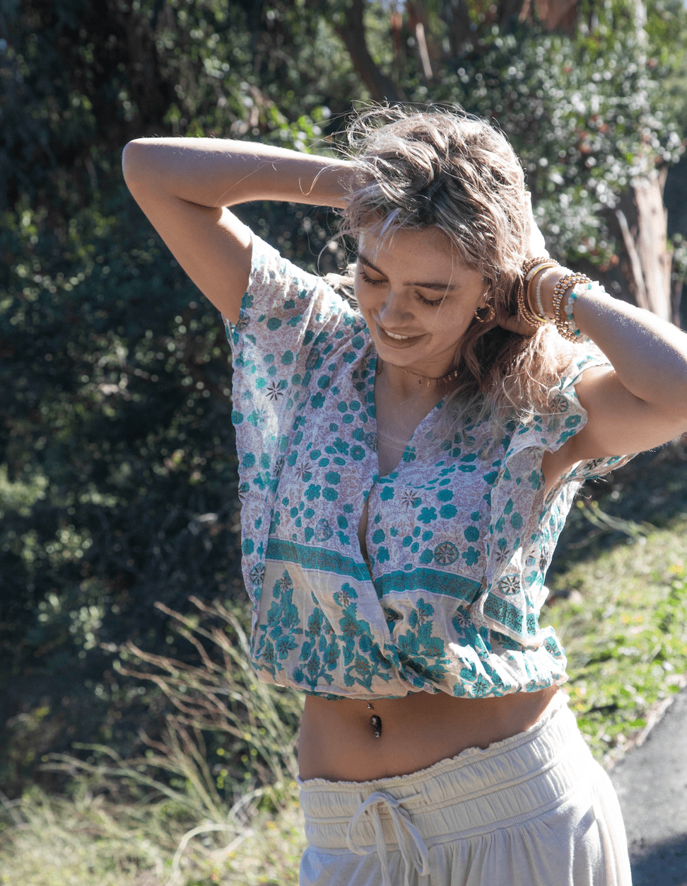 Woman in a floral top and white skirt standing outdoors with greenery in the background