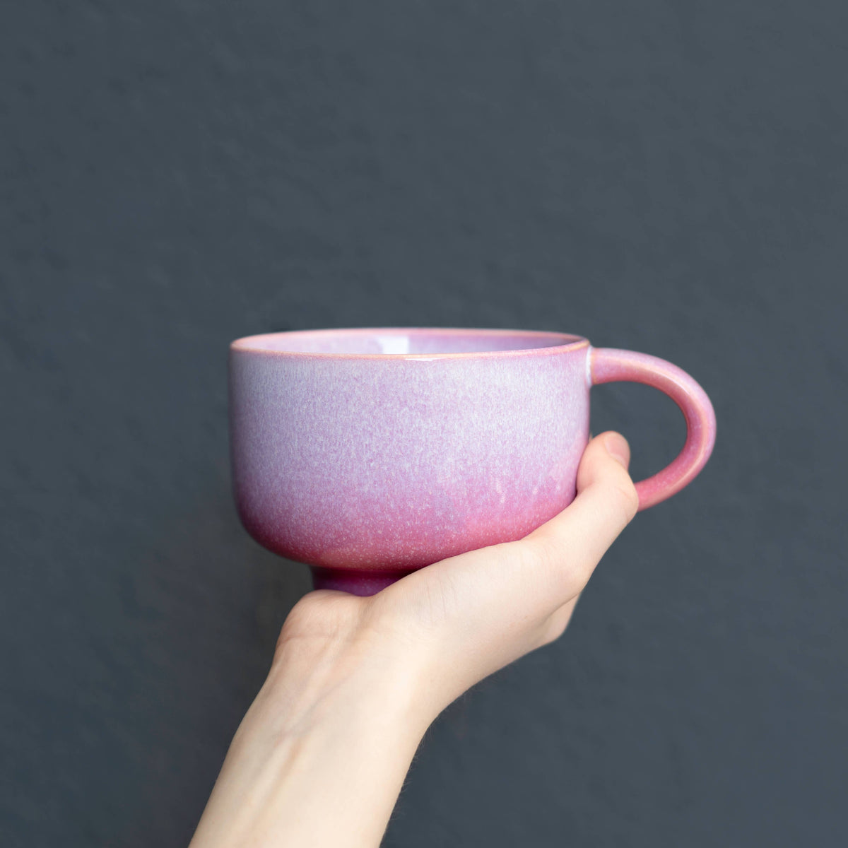 Hand holding a pink speckled mug against a dark background
