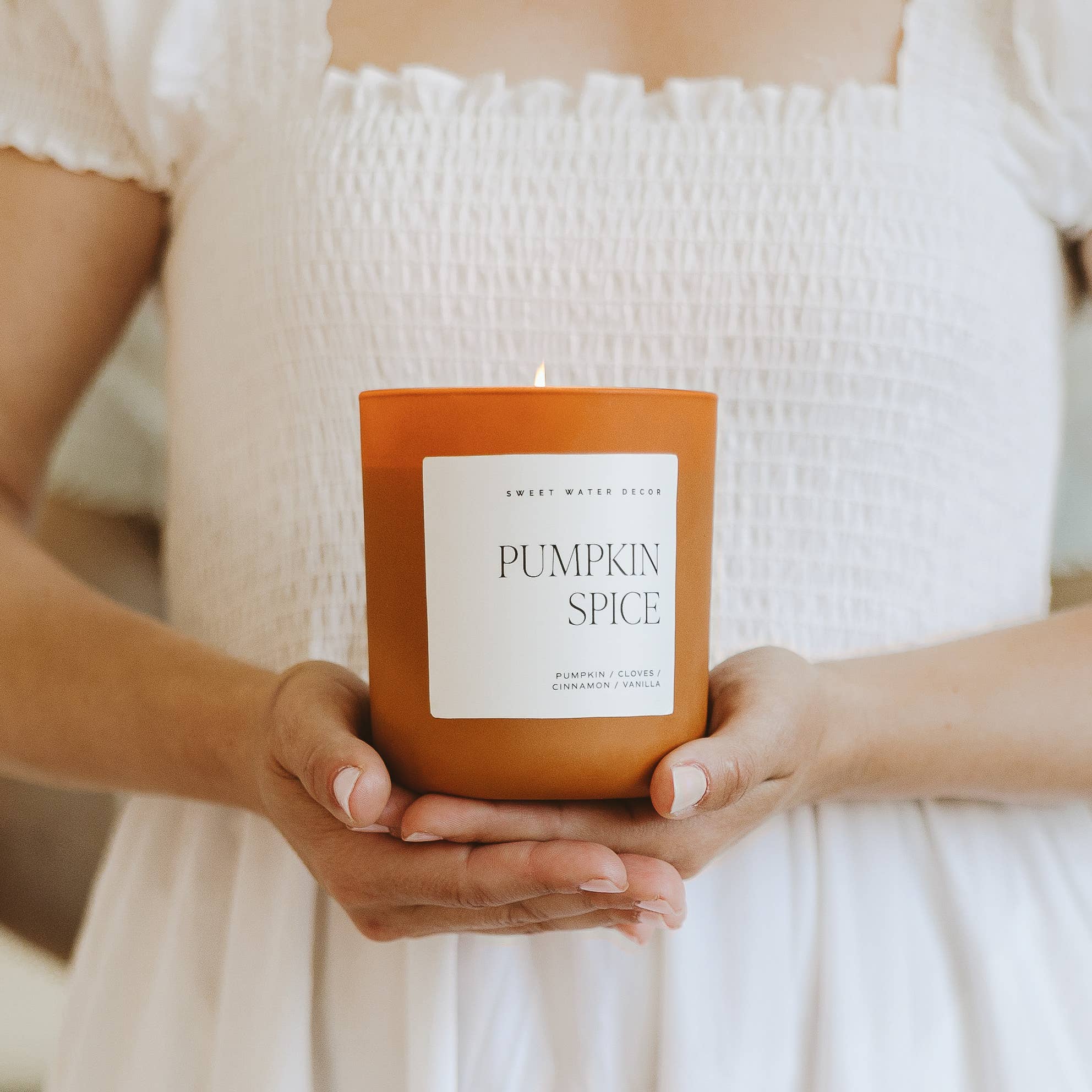 Person holding a 'Pumpkin Spice' candle with a blurred background