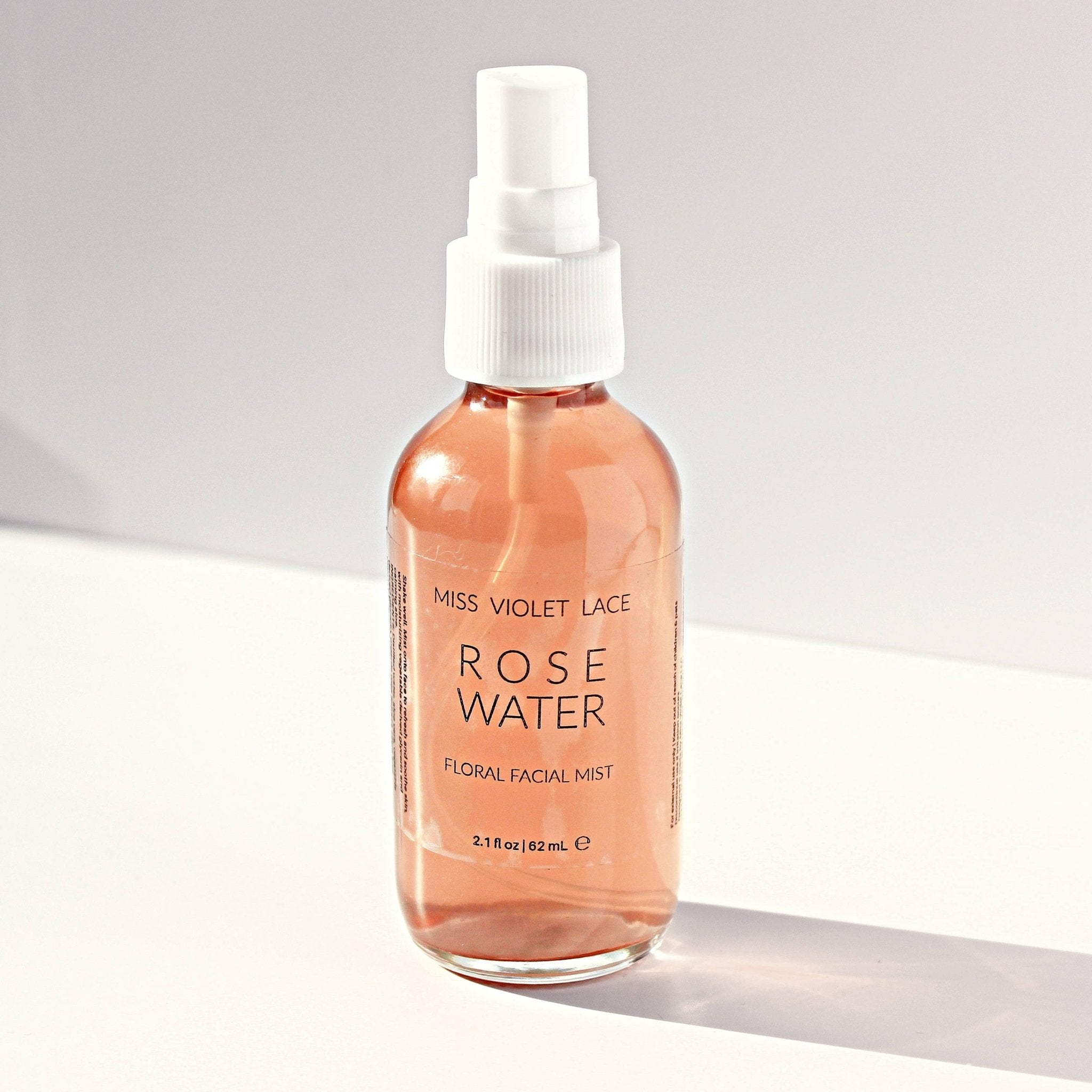 Miss Violet Lace Rose Water Floral Facial Mist, 2.1 fl oz, in a clear bottle with pink liquid and white spray top