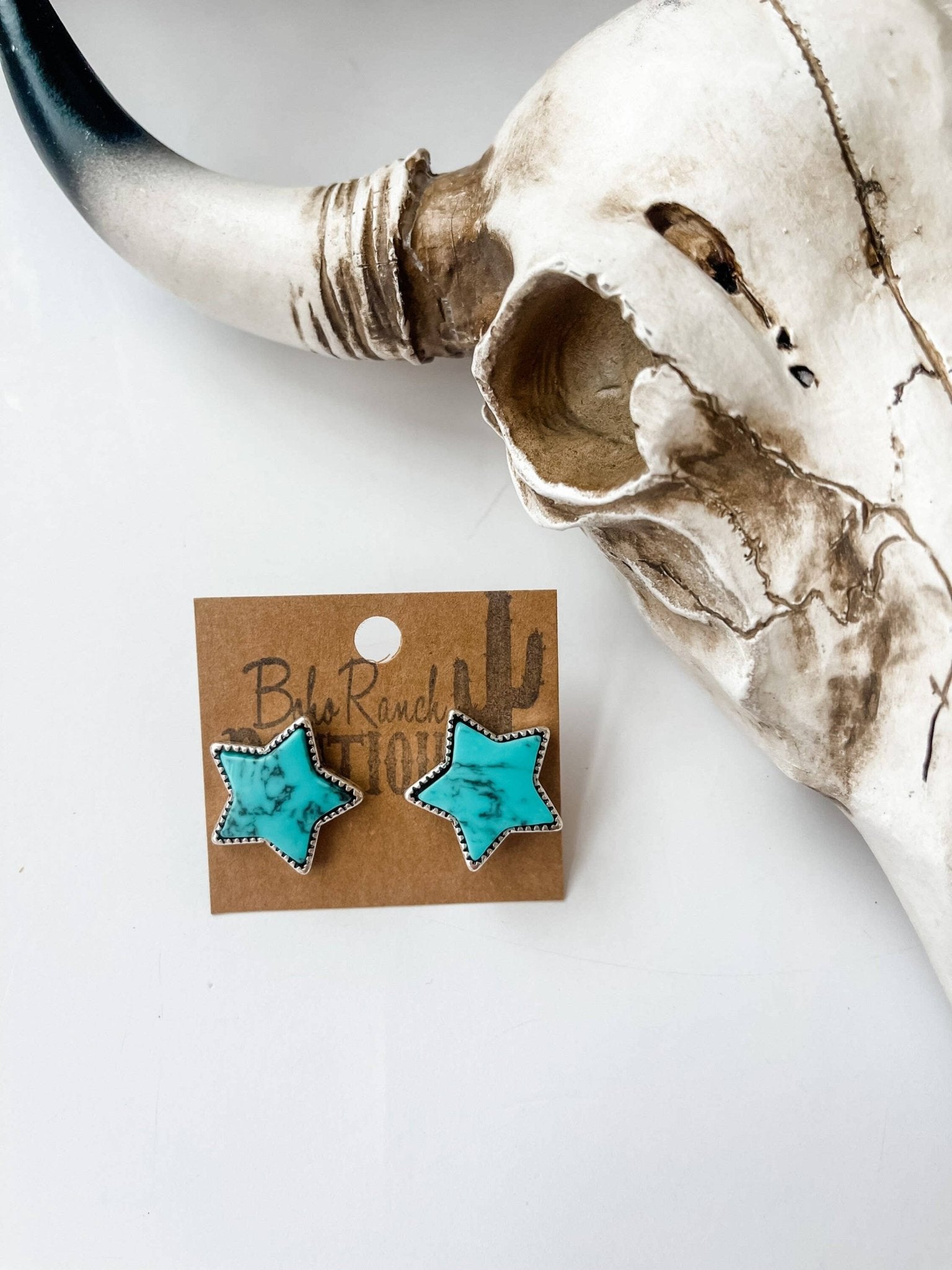 Turquoise star earrings on a card with a skull in the background