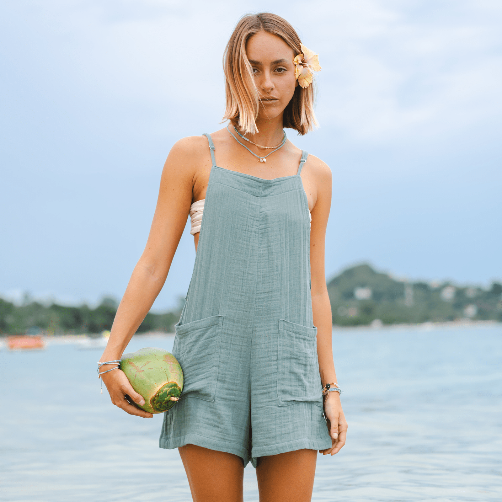 Women's sage green crinkled cotton romper with adjustable straps and large pockets, styled for summer beachwear