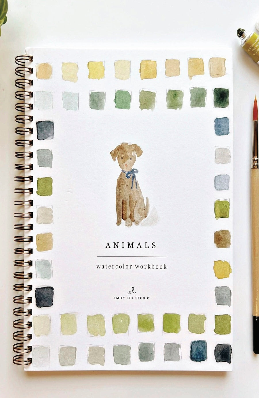 A spiral-bound watercolor workbook titled 'Animals' with a painted dog illustration in the center and a border of watercolor color swatches around the cover. A paintbrush and part of a paint tube are visible at the top right on a white background.