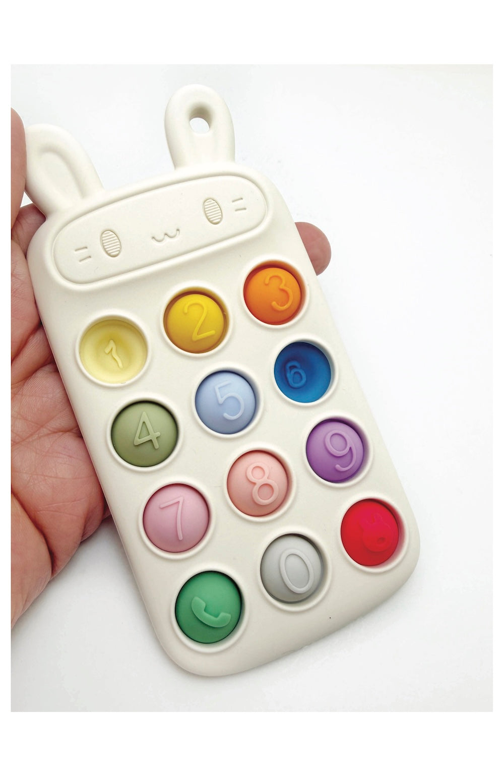 A hand holding a white silicone baby teething toy shaped like a bunny phone with colorful numbered buttons.