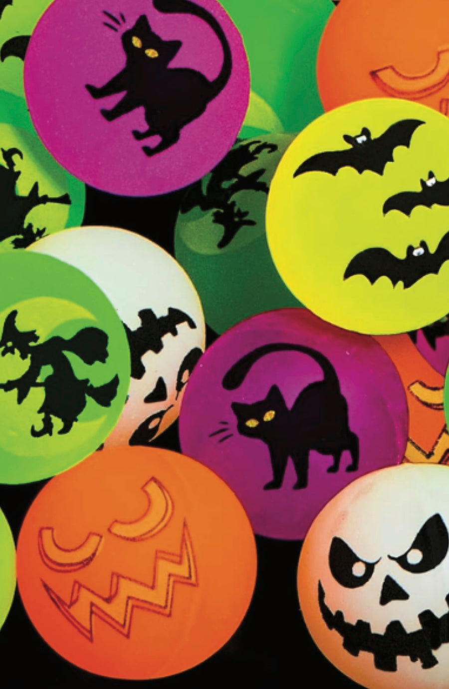 A close-up arrangement of round Halloween-themed glow in the dark bouncy ball in bright neon colors, including black cat silhouettes on purple, bats on yellow, jack-o'-lantern faces on orange, a witch silhouette on green, and a spooky face on white.