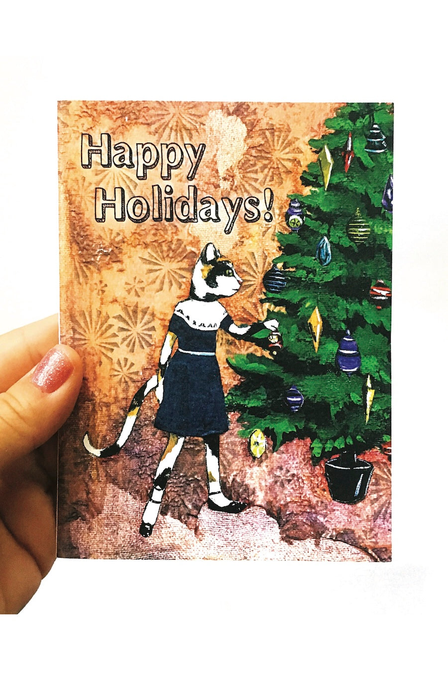 A hand holding a square Christmas greeting card with a whimsical illustration of a cat in a black dress decorating a Christmas tree, with the text 'Happy Holidays!' on a white background.