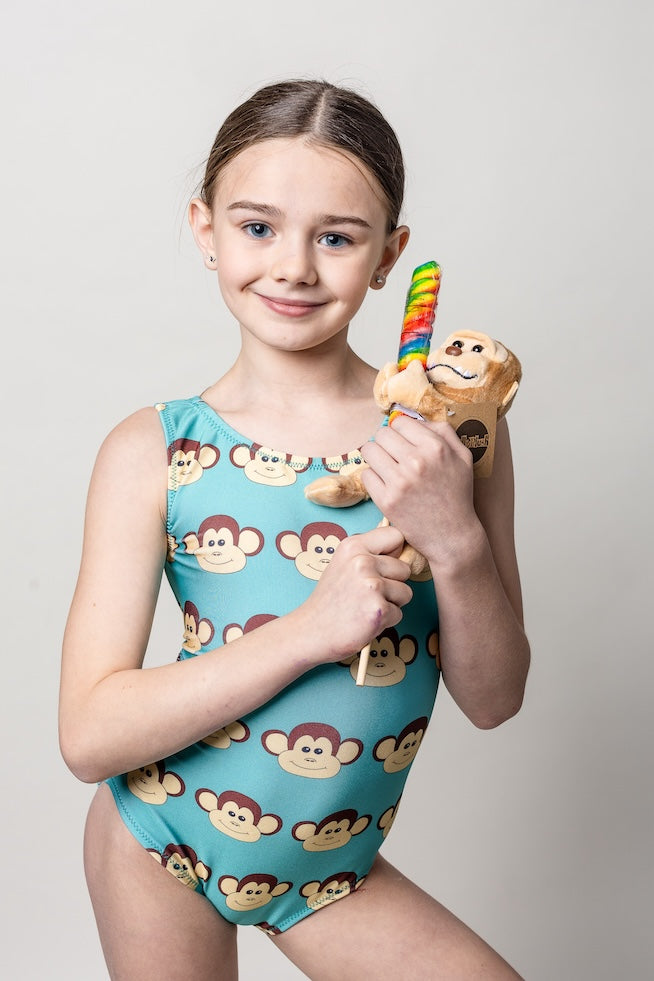 Young girl in a teal monkey-patterned gymnastics leotard holding a sucker with a rainbow and monkey plushie