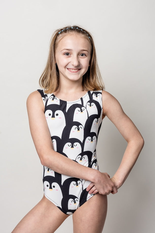 Young girl wearing a black and white penguin-patterned leotard for gymnastics on a plain background