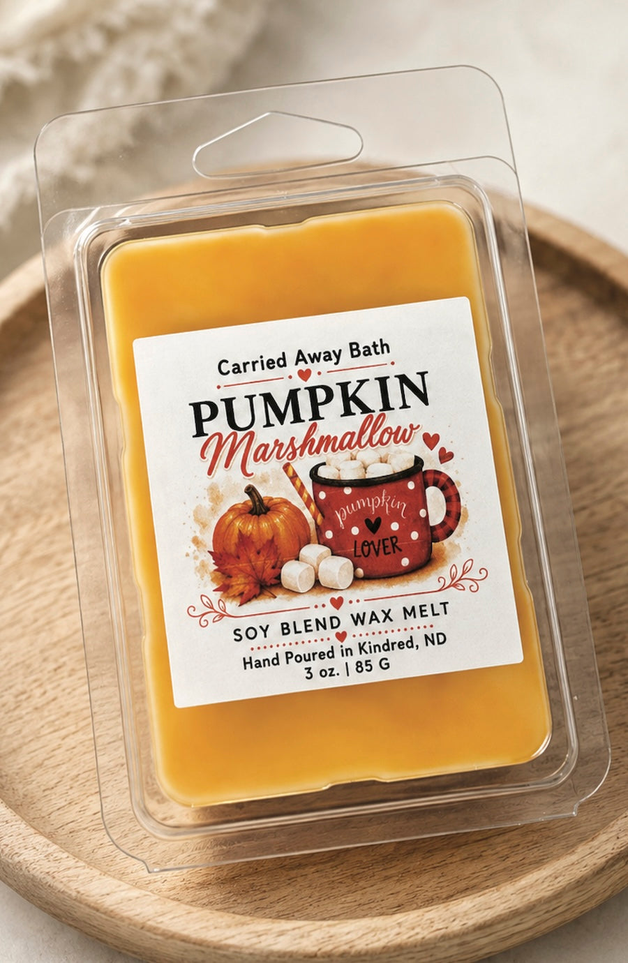 Carried Away Bath Pumpkin Marshmallow soy blend wax melt in a clear clamshell package, resting on a round wooden tray.