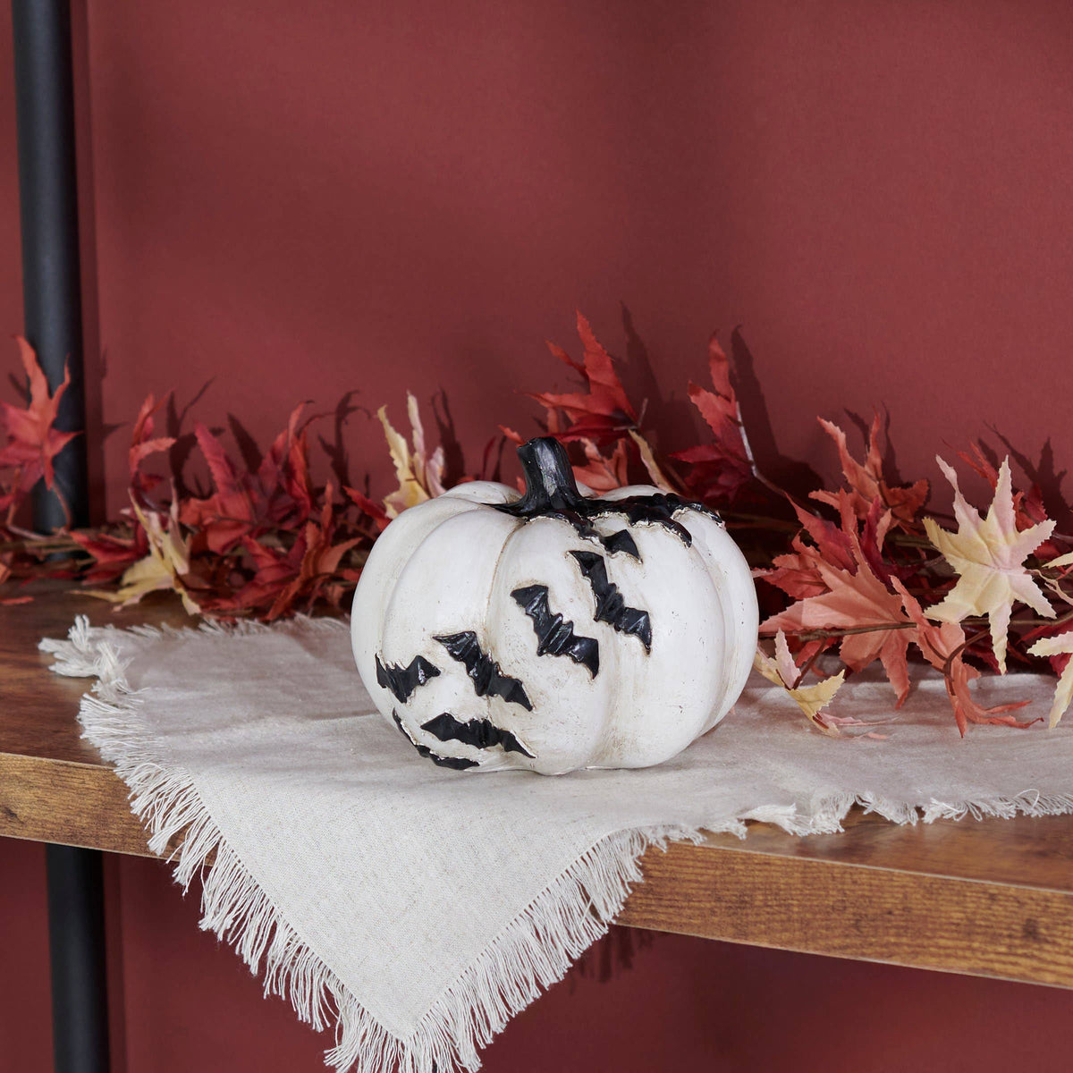 Decorative white pumpkin with black bat designs on a wooden surface with fall leaves in the background.