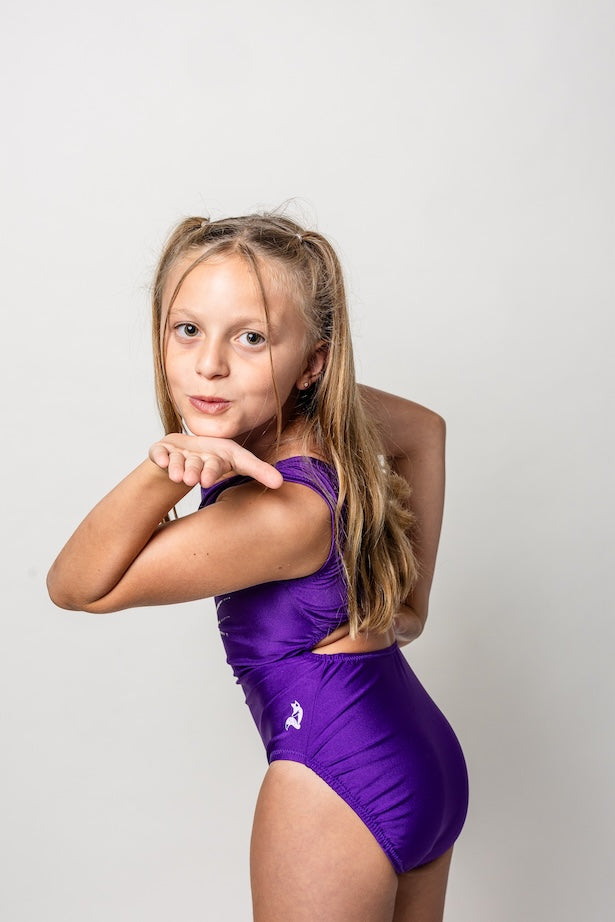Young gymnast wearing a purple open-back bling leotard with a white background